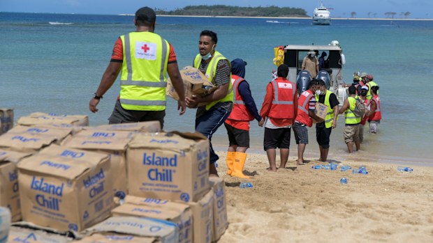 In this photo provided by Malau Media/IFRC, Tonga Red Cross Society's staff and volunteers unloading boxes of water bottles from the boat into the beach in Nomuka Ha'apai Island, Tonga on April 1, 2022. Three months on from a devastating volcano and tsunami in Tonga, the AP checks in on how the island nation is recovering. The bill from the tsunami is estimated at some $90 million and GDP is expected to fall by more than 7% this year. The cleanup has been hindered by an internet outage caused by