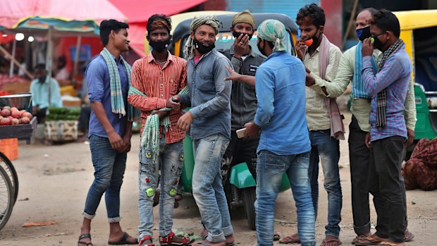 Daily wage laborers wearing face masks as a precaution against the coronavirus stand together as they wait for work at a wholesale market in Bengaluru, India, 