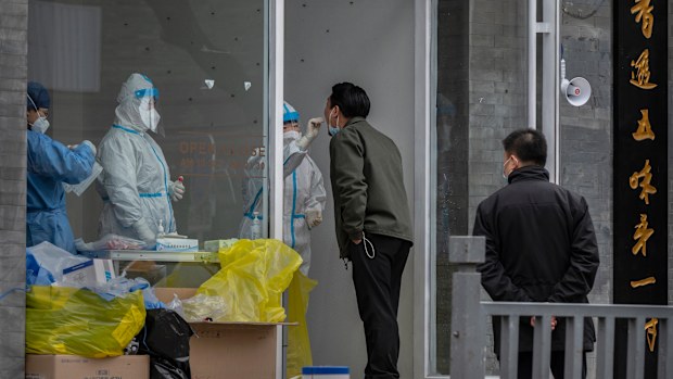BEIJING, CHINA - MARCH 25: A health worker wears a protective suit as she performs a nucleic acid test to detect COVID-19 on a local resident at a pop-up testing site in the street on March 25, 2022 in Beijing, China. China has stepped up efforts to control a recent surge in coronavirus cases across the country, locking down the entire province of Jilin and the city of Shenyang and putting others like Shenzhen and Shanghai under restrictions. Local authorities across the country are mass testing
