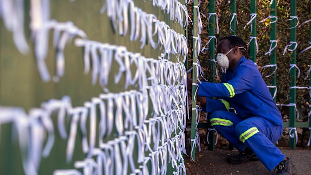 In this July 29, 2020 photo, Silva Cossa, the caretaker, ties ribbons onto the fence to represents a South African who has died from COVID-19, at St James Presbyterian church in Bedford Gardens, Johannesburg, South Africa. 
