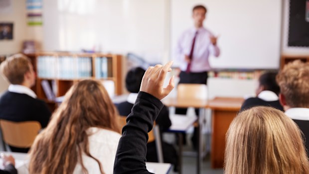 Female Student Raising Hand To Ask Question In Classroom