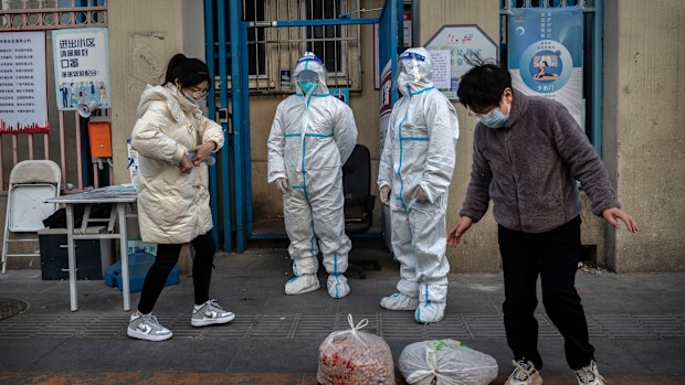 An epidemic control worker and a security guard wear protective suits to prevent the spread of COVID-19 as a resident collects a food order outside an apartment building in the Central Business District on November 26, 2022 in Beijing, China. 
