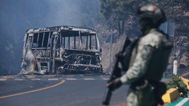 A soldier stands guard by a charred vehicle after it was set on fire, in Cointzio, Michoacán state, Mexico, Sunday, Feb. 22, 2026, following the death of the leader of the Jalisco New Generation Cartel, Nemesio Oseguera, known as "El Mencho."  