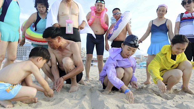 People look at children writing letters, "our fatherland," on the beach at the Wonsan-Kalma resort in Wonsan, Kangwon Province, North Korea, Wednesday, July 2, 2025. (AP Photo/Jon Chol Jin)