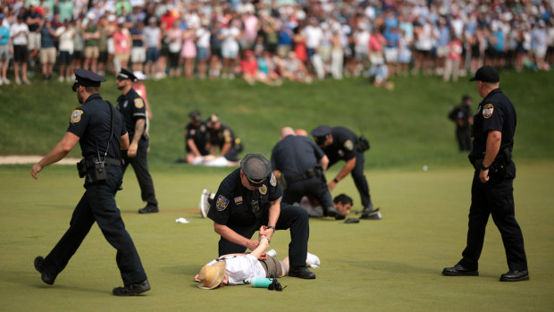 Climate protestors are ushered off the 18th green by police officers during the final round of the Travelers Championship.