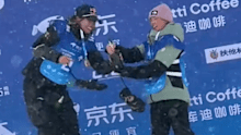 Eileen Gu leans over to help Indra Brown crack a bottle of champagne on the podium.