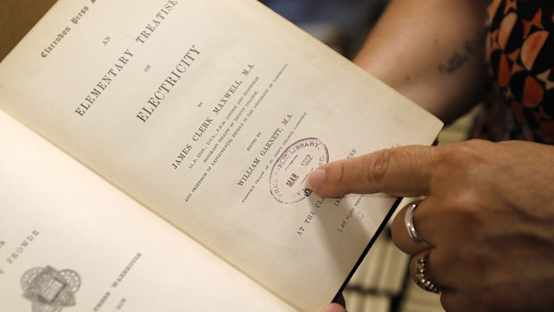 New Bedford Public Library Director Olivia Melo, points to a stamp dating to 1882 when the New Bedford library system acquired the book, on Friday, July 7, 2023, in New Bedford, Mass. "An Elementary Treatise on Electricity" by James Clerk Maxwell was last checked out about 119 years ago, has been returned to the Massachusetts library after it was discovered among books donated to the libraries at West Virginia University.