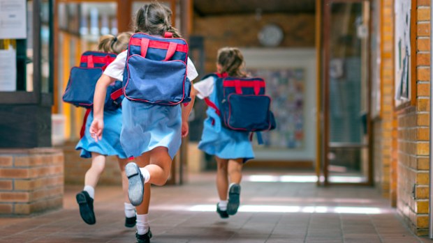 Rear view of excited students running towards entrance. Girls are carrying backpacks while leaving from school. Happy friends are wearing school uniforms.