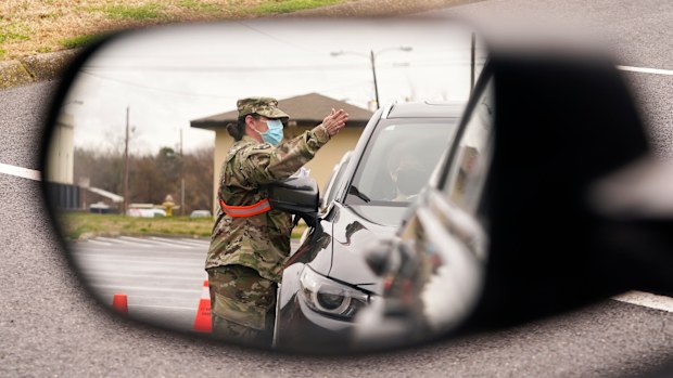 A National Guard soldier directing drivers is reflected in the mirror of a car waiting in a COVID-19 vaccination line  in Shelbyville, Tennessee.