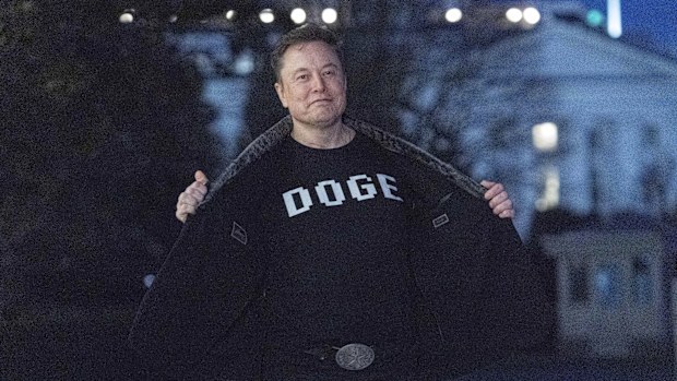 Elon Musk flashes his t-shirt that reads "DOGE" to the media as he walks on South Lawn of the White House, in Washington, Sunday, March 9, 2025.