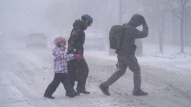 The Firestone family makes their way across Elmwood Avenue in Buffalo, N.Y. after stocking up on supplies at the grocery store, Friday, Dec. 23, 2022. Winter weather is blanketing the U.S. as a massive storm sent temperatures crashing and created whiteout conditions.(Derek Gee /The Buffalo News via AP)