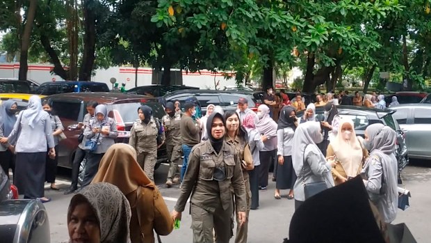 People wait outside after they evacuate a government building following an earthquake, in Makassar, South Sulawesi, Indonesia. 