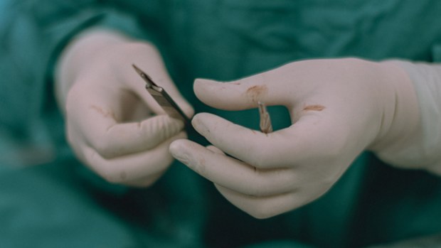 Unrecognizable female nurse prepares a surgical scalpel to hand to the surgeon an operation.