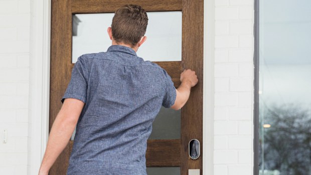A mid adult male grocery delivery person knocks on door of a customer's home. Paper bags filled with groceries are on the front stoop.