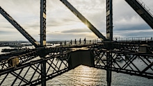 <p>Sydney Harbour Bridge's BridgeClimb has announced its first major suit redesign in over 12 years.</p><p>Created in collaboration with First Nations' artist Taleena Simon, the design reflects Gadigal Country, showcasing whales, fisherwomen in Nawi canoes, and gathering circles symbolising shared climber experiences.﻿</p><p>"I wanted to create a piece that not only celebrates the beauty of the landscape but also honours the ancestral connections ﻿and stories of the Indigenous peoples who have called this land home for millennia," said Simon, who is a proud Worimi and Bundjalung woman.</p>