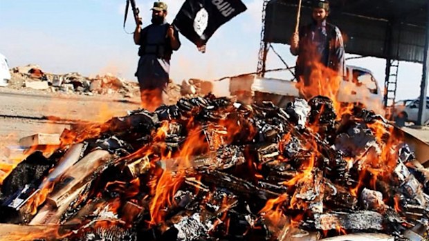 A jihadist waves the ISIS flag as the banned goods burn.