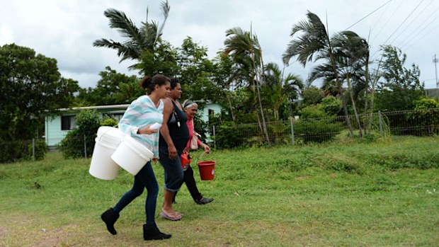 Local residents walk holding buckets and a jerrican for storing water and fuel ahead of the arrival of cyclone Ita in Cooktown. (AAP)