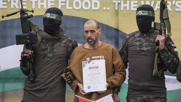 Israeli captive, Eli Sharabi, who has been held hostage by Hamas in Gaza since October 7, 2023, stands on a stage escorted by Hamas fighters before being handed over to the Red Cross.
