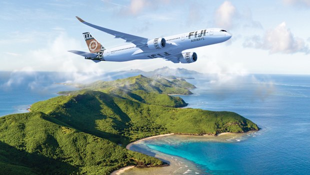 A Fiji Airways plane flying over an island and blue sea.