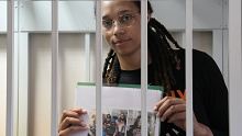 Brittney Griner holds up images from within a courtroom cage.