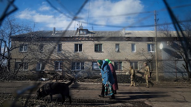 Two Ukrainian soldiers patrol a street as elderly women walk past a house damaged by artillery shelling in Novoluhanske, eastern Ukraine amid the threat of a Russian invasion. 