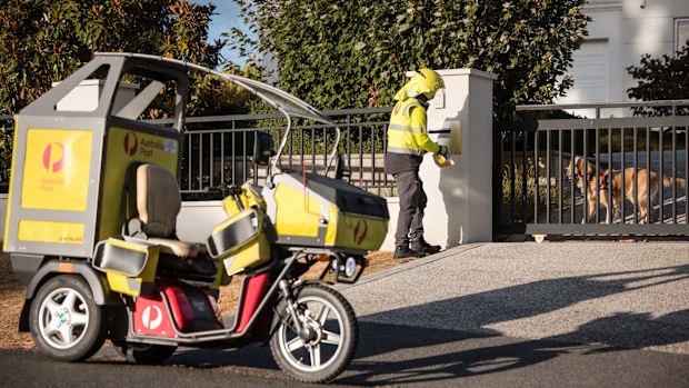 An Australia Post Postie delivers mail to a house with a dog.
