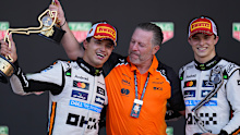 McLaren driver Lando Norris celebrates on the podium with McLaren CEO Zak Brown and teammate Oscar Piastri.