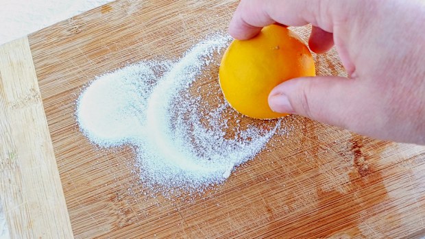 Woman's hand cleaning cutting board with lemon and salt