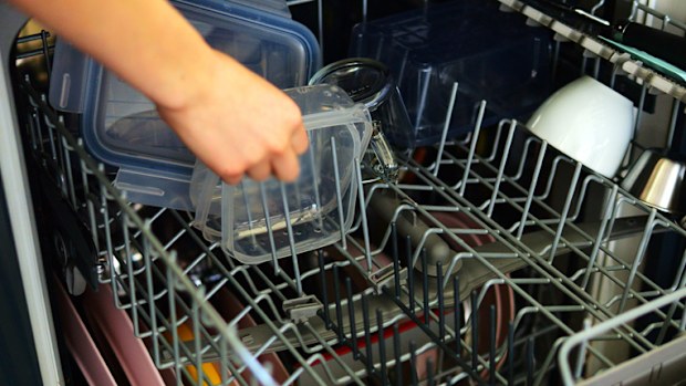 Housewife takes wet container out of open dishwashing machine at home closeup. Woman uses automatic appliance to clean dirty dishes in kitchen