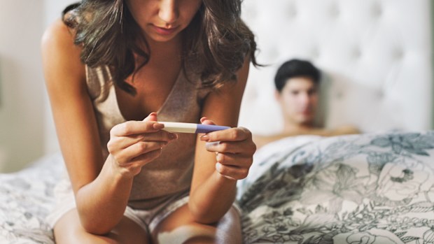 Shot of a woman taking a pregnancy test at home with her boyfriend lying in the background