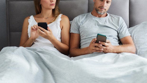 Mid adult couple using mobile phones in a bed while woman is peeking into her husband's phone. cheating affair infidelity