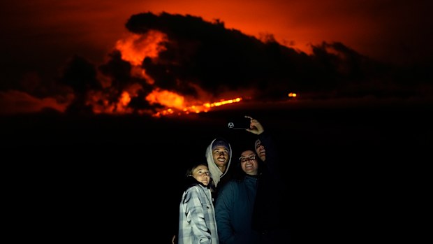 Ashlyn Nadeau, left, stands next to her husband, Casey Nadeau, second from left; Jessica Doyle, second from right, and Justin Potter, right, as they take a picture below the Mauna Loa volcano as it erupts Friday, December 2, 2022, near Hilo, Hawaii.