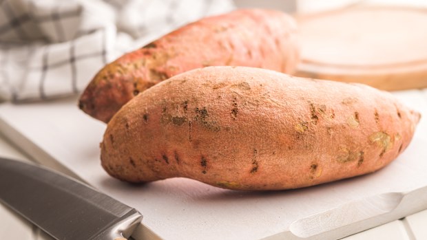 Raw sweet potatoes on cutting board on a white table.