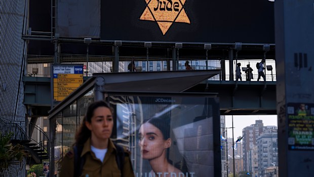 People walk along a bridge lit with a billboard showing a yellow Star of David that reads "Jude", Jew in German, resembling the one Jews were forced to wear in Nazi Germany, during the annual Holocaust Remembrance Day in Ramat Gan, Israel.