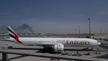 ADDS CAUSE OF BLACK SMOKE IN THE BACKGROUND.- A plume of smoke caused by an Iranian strike is seen in the background an an Emirates plane is parked at the Dubai International Airport after its closure in Dubai, United Arab Emirates, Sunday, March 1, 2026. (AP Photo/Altaf Qadri)