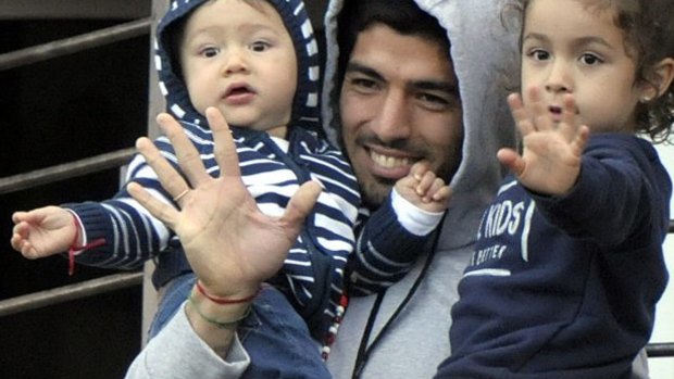 Luis Suarez holds his children as he greets fans from their home's balcony on the outskirts of Montevideo.