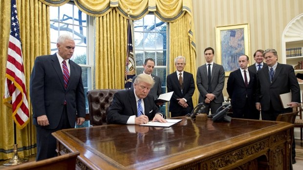 Surrounded by male advisers, Donald Trump signs an executive order banning aid to organisations that discuss abortion.  