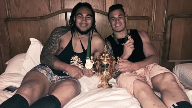 Ma'a Nonu and Sonny Bill Williams lie on a hotel bed with the Webb Ellis Cup.