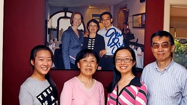 The Wang family in their Altona home, in front of a photograph of Julia Gillard and Jian and Zheng Wang.