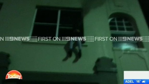 The woman is shown in the footage sitting on the windowsill, as fire leaps out the side of the building.
