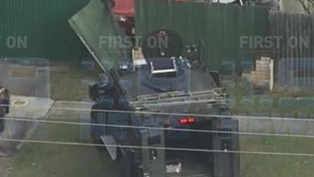 Police use an armoured vehicle to break down the gate of house under siege at Redcliffe.