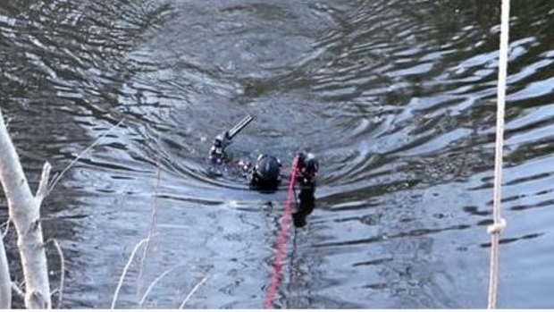 A police diver emerges from the Queanbeyan River holding a gun.