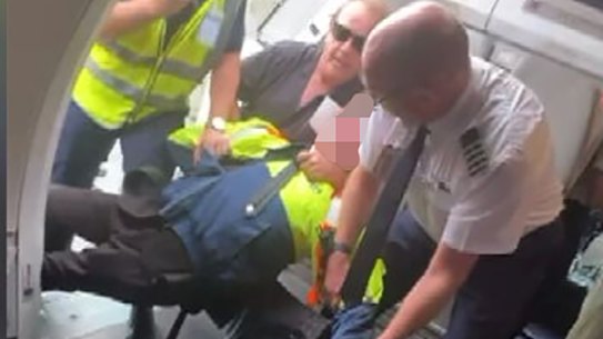 A still from footage of the boy being restrained by a Jetstar worker, passenger Barry Clark and the pilot.
