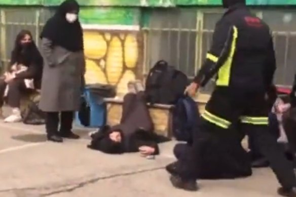 A girl awaits medical assistance after falling ill outside a school in Iran.