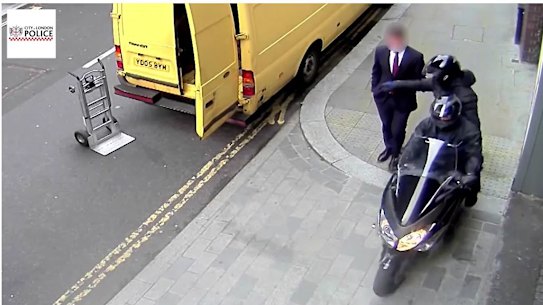 A thief steals a mobile phone from a man as he walks down a London street.
