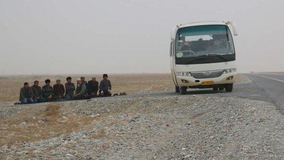 Uighur men stop their bus on the roadside to pray on a highway leading into Hotan in Xinjiang.