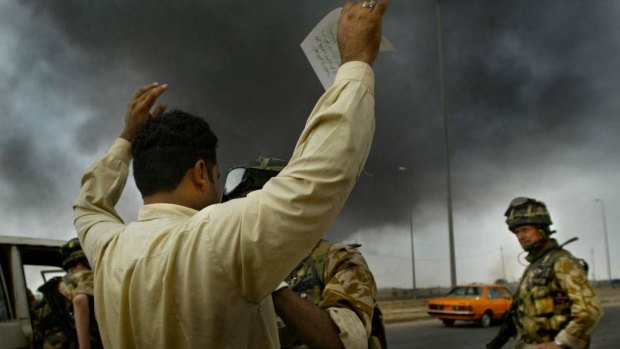 Searched by British soldiers, an Iraqi man on the outskirts of Basra holds his arms in the air clutching a leaflet written by the Coalition forces stating “People of Basra we are here to liberate the people of Iraq”.