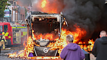 People watch as firemen arrive to put out vehicle that was set alight during a protest in East Belfast.