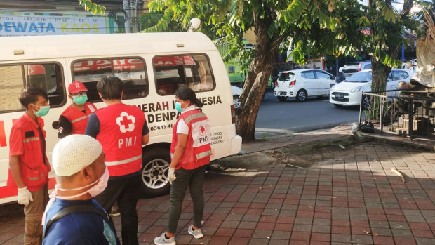 French tourist Gerard Philippe Follet, 72, slumped over his scooter, unconscious, on Bali's Jalan Iman Bonjol as ambulance workers wait for medical officers equipped to deal with a coronavirus patient.