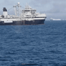 A whale breaches in the Antarctic near a krill trawler.